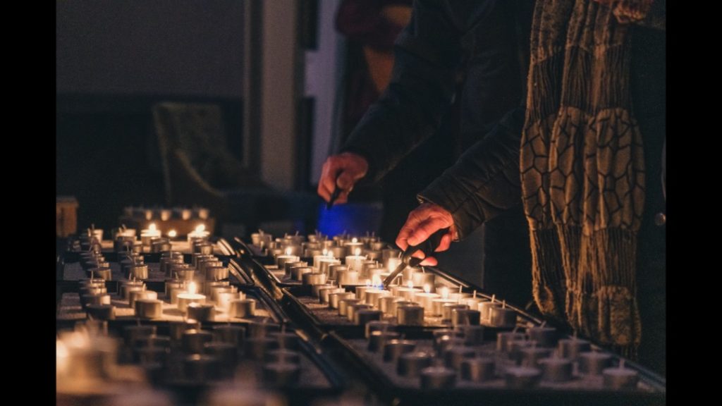 Aansteken van kaarsjes tijdens Lichtjesavond 2025 Zichtbaar zijn een verzameling waxinelichtjes en 2 handen met een aansteker die de handeling van het aansteken uitvoeren.