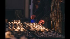 Aansteken van kaarsjes tijdens Lichtjesavond 2025 Zichtbaar zijn een verzameling waxinelichtjes en 2 handen met een aansteker die de handeling van het aansteken uitvoeren.